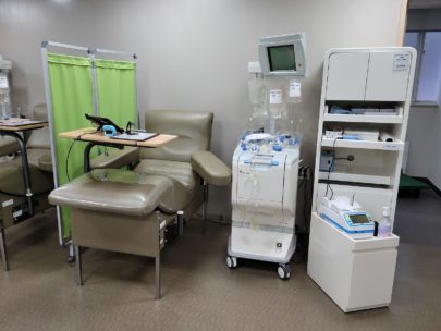 a room with a blood donation chair/bed, a green privacy screen, and some medical equipment